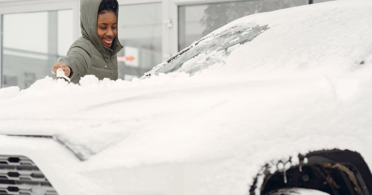 Person removing snow from a car during winter outdoors
