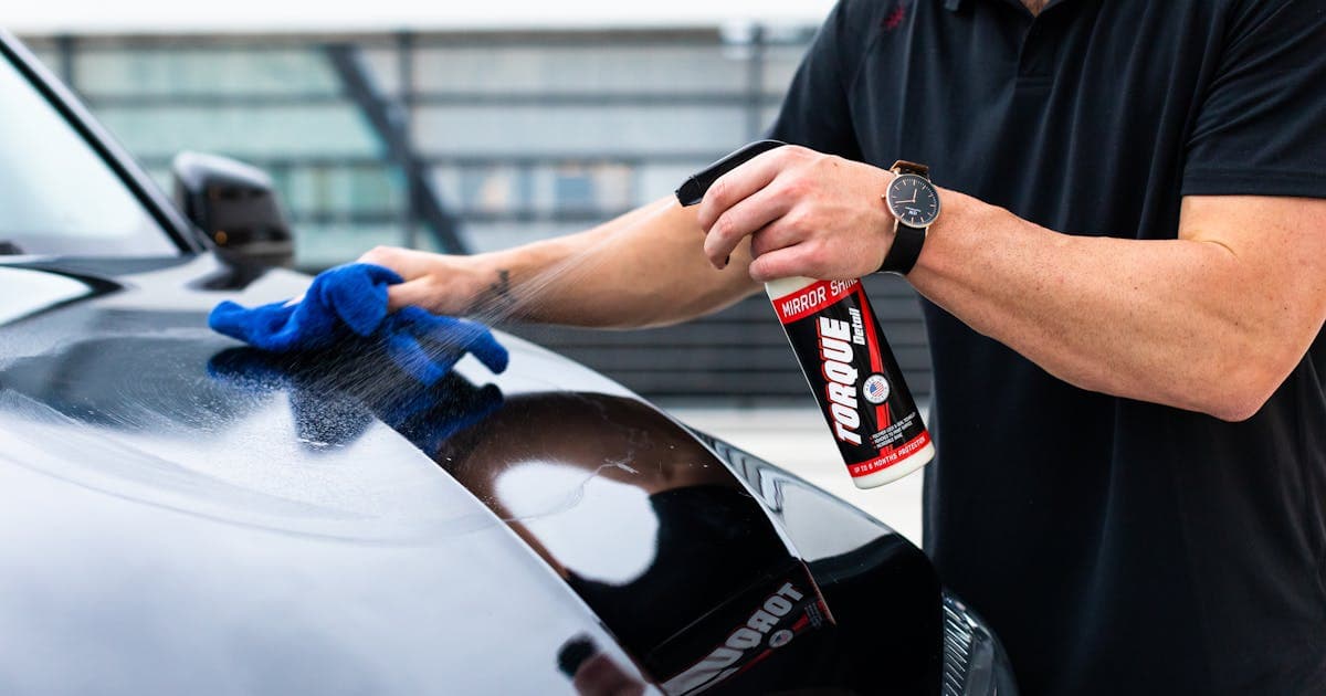 Professional detailer applying protective coating to a car hood with a microfiber cloth