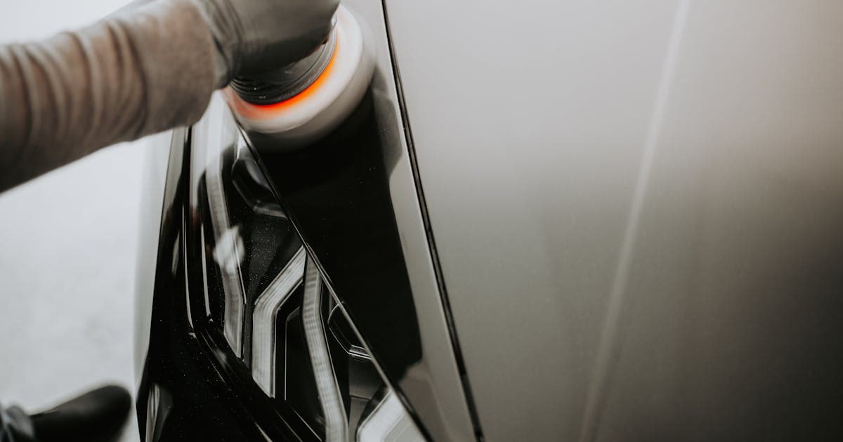Close-up of a professional detailer polishing a black car with a buffing machine